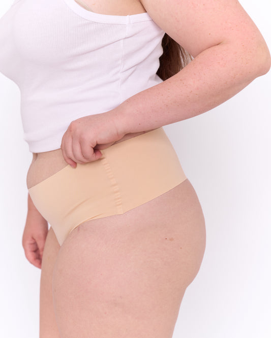 Close up side view of a woman modelling Trelou's active underwear, wearing a white tank top.